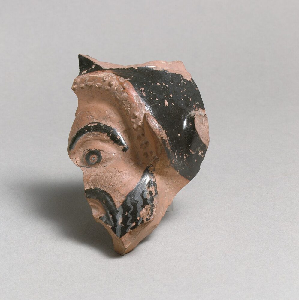 Greek terracotta vase fragment modelled as a satyr's head, showing the snub nose, pointed ear and beard, ca. 5th century BCE.